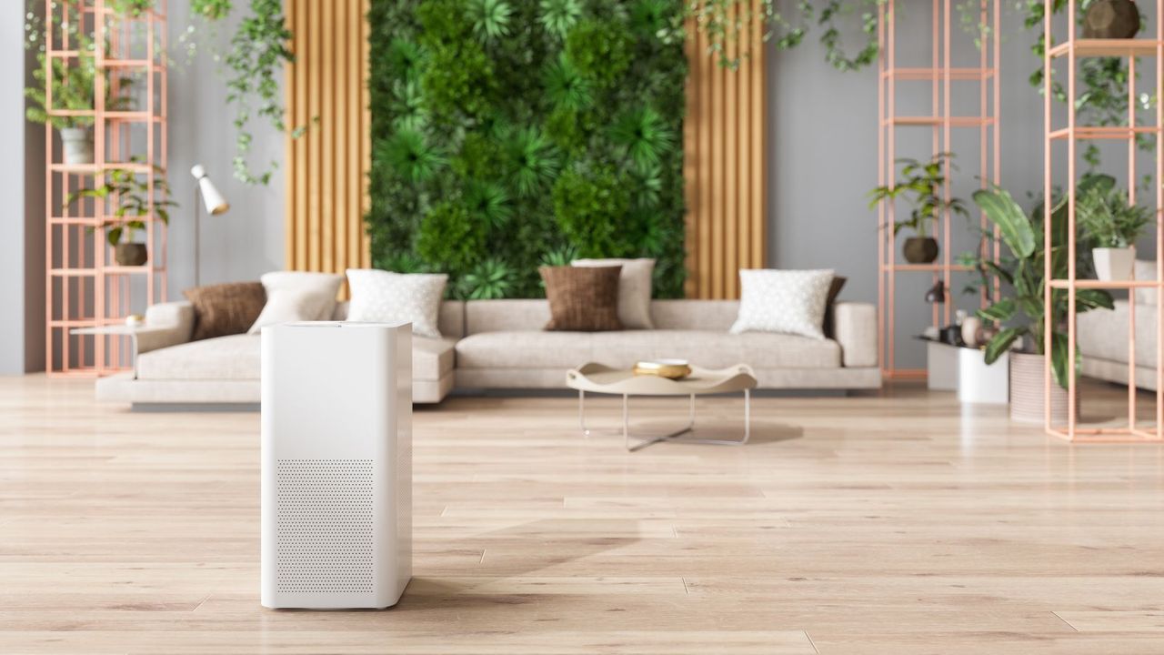 a white air purifier fan is in the middle of a lounge with wooden floors and plants on the walls