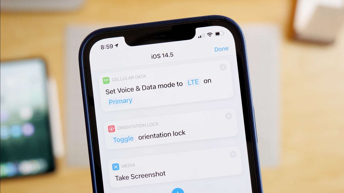 Hero photo of Shortcuts actions new in iOS 14.5 – Set Voice &amp;amp; Data Mode, Set Orientation Lock, and Take Screenshot running on an iPhone above a desk with an iPad, Mac mini, and notecards on the 