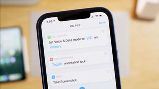 Hero photo of Shortcuts actions new in iOS 14.5 – Set Voice & Data Mode, Set Orientation Lock, and Take Screenshot running on an iPhone above a desk with an iPad, Mac mini, and notecards on the 
