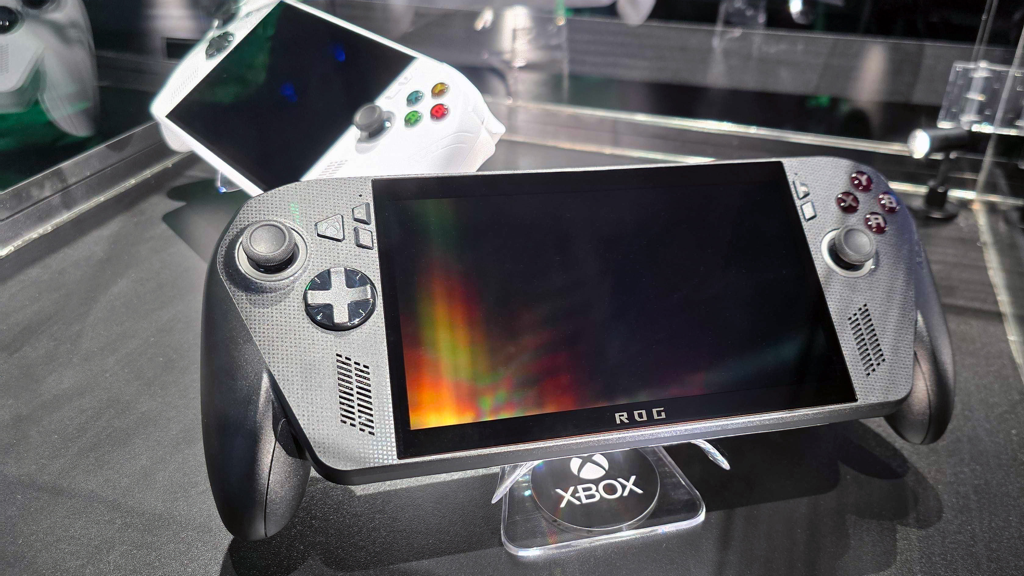 ASUS ROG Xbox Ally X (black) and ROG Xbox Ally (white) in a glass display case at Gamescom in August, 2025.