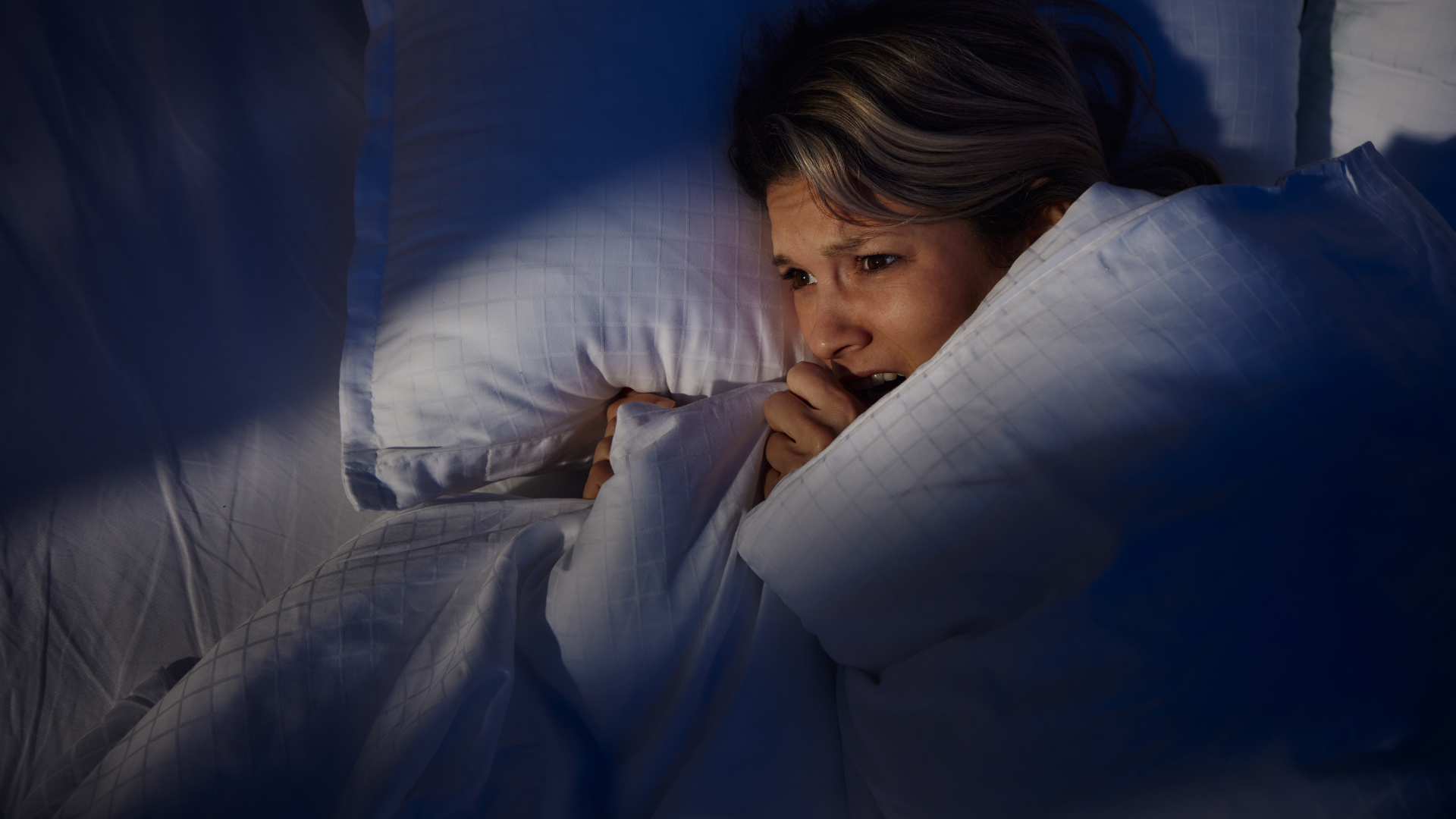 A woman lying awake on her side in bed at night looking anxious.