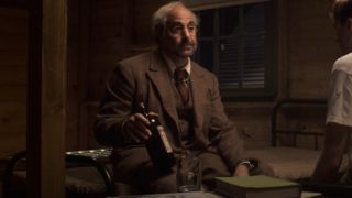 Stanley Tucci sits sternly while showing off a bottle he brought in Captain America: The First Avenger.