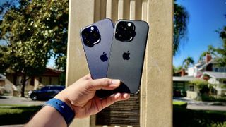 Someone holding two iPhone 14 Pro models next to each other outside.