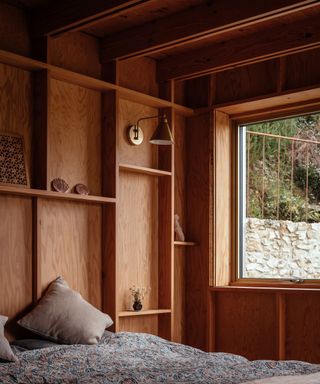 The bedroom has a large window overlooking a stone wall and timber cladded walls
