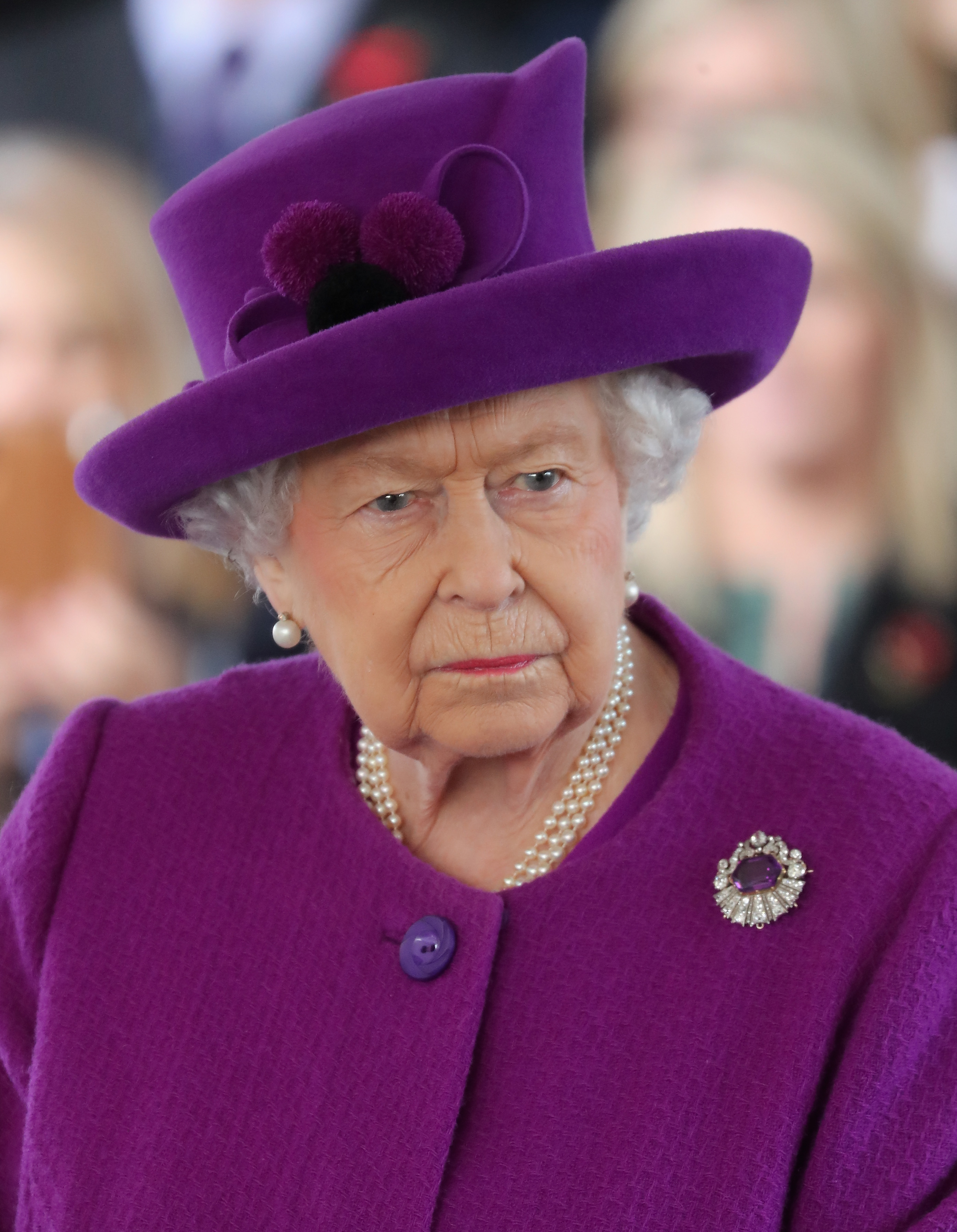 Queen Elizabeth wearing a purple coat and hat and scowling