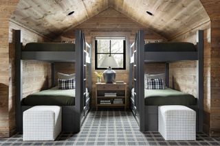 double bunk room in cabin style with chequered carpet pillows and ottomans set under the eaves in wood paneled space