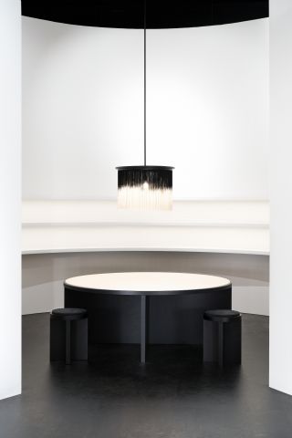 A round white topped table and black stools below a black and white vignetted chandelier.