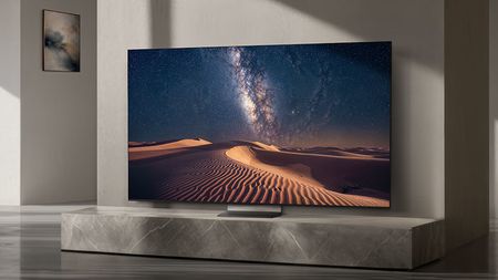 The Samsung R95H in a gray-colored living room displaying the Milky Way over sand dunes in the desert