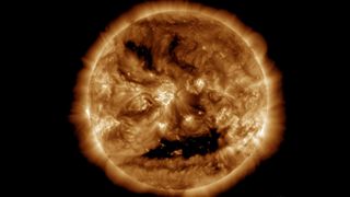 close up view of the sun with two bright "eyes" and a large coronal hole that looks like a smiling mouth.