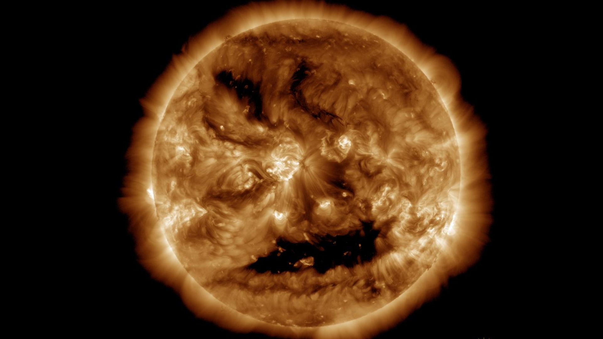 close up view of the sun with two bright "eyes" and a large coronal hole that looks like a smiling mouth.