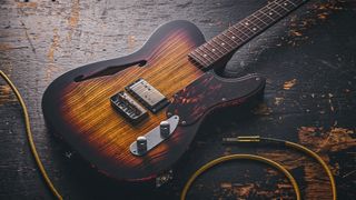 Patrick James Eggle Oz-t Cabronita Thinline; this semi-hollow T-style has a dark sunburst that reveals all the open grain, complementing the tortoiseshell pickguard, and is photographed here against a distressed floor, white and wooden backgrounds.