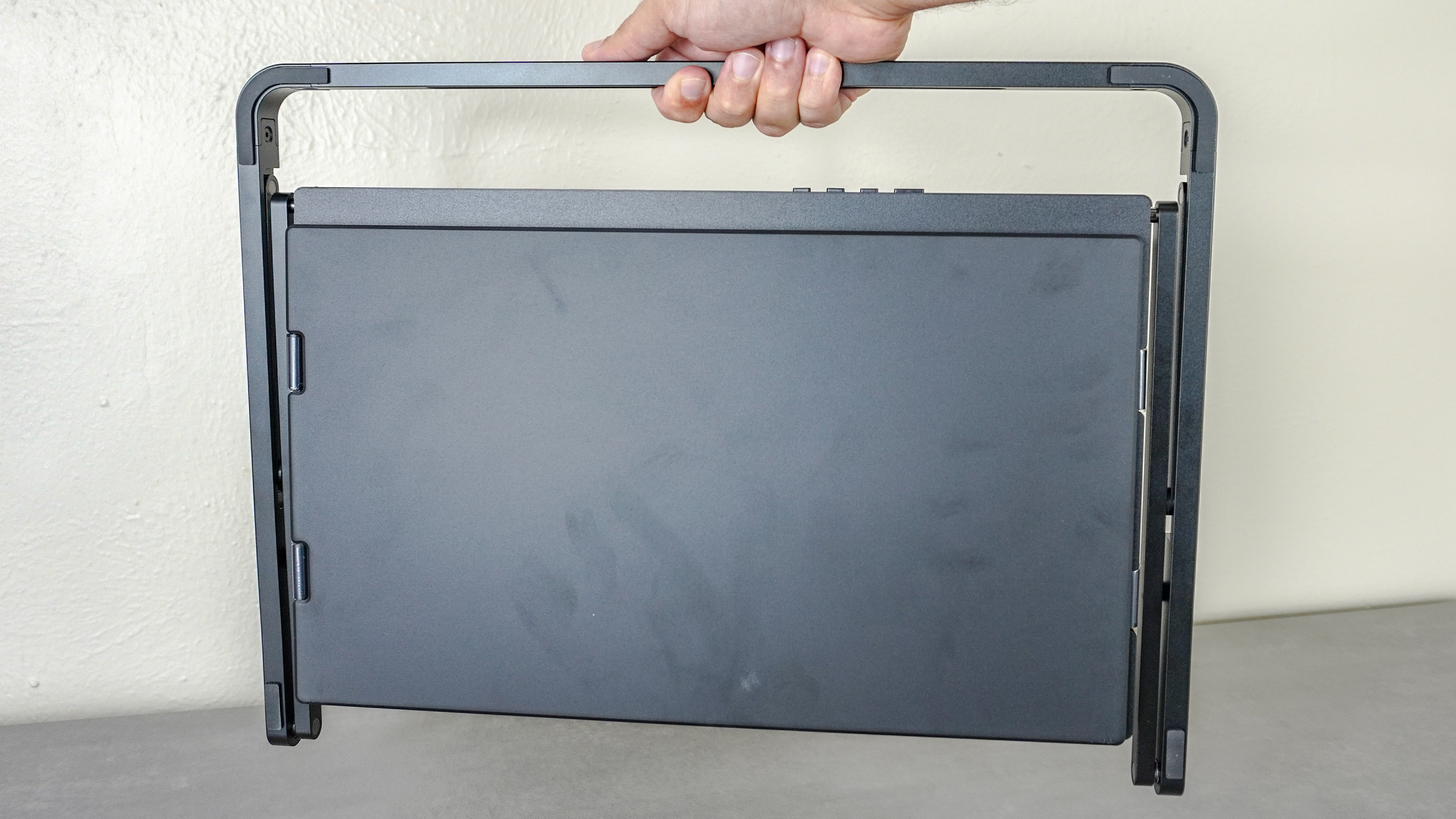 A person holding the Aura Triple Aero 15.6 Pro Max portable monitor by its built-in handle