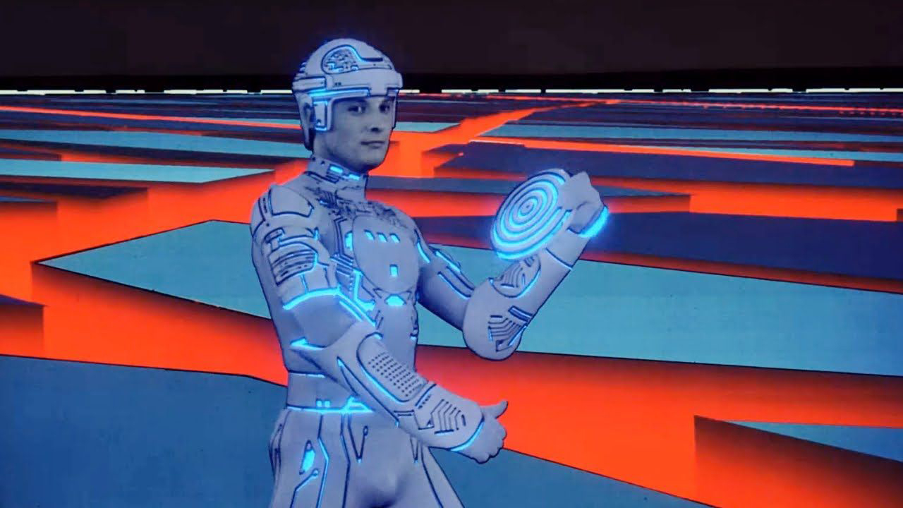 Screenshot from the movie Tron. A person is wearing a white bodysuit and helmet, both with blue light trim. They are holding up a disc with a blue spiral on it, preparing to throw it.