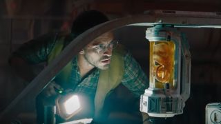 Jonathan Bailey curiously examines a dinosaur embryo by flashlight in Jurassic World Rebirth.