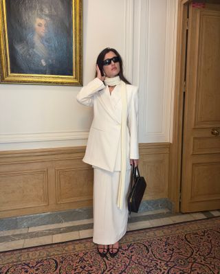 Ilirida Krasniqi wearing a white blazer, scarf, and skirt with black sandals and a black bag.