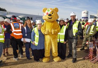 Pudsey Bear gives two thumbs up on the building site of this year's DIY SOS Children In Need special. Surrounding him, all in high-vis jackets and hard hats, are designer Gaby Blackman, Flavia and Sharan from the charity Getaway Girls, and presenter Nick Knowles