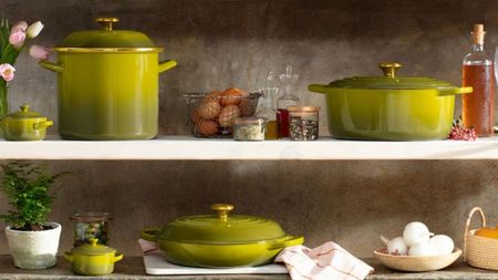 The Le Creuset Olive cookware collection on white kitchen shelves. 