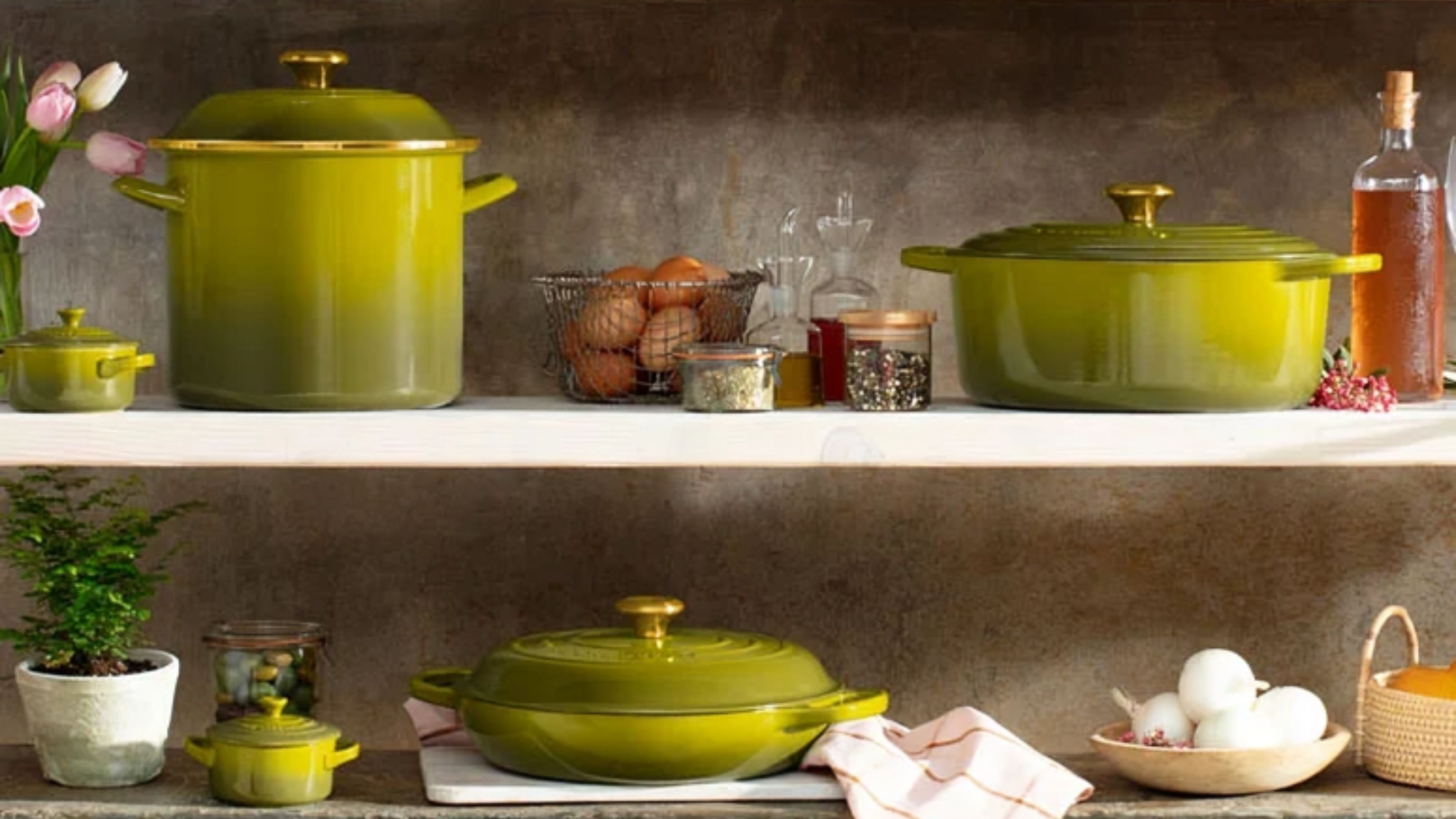 The Le Creuset Olive cookware collection on white kitchen shelves. 