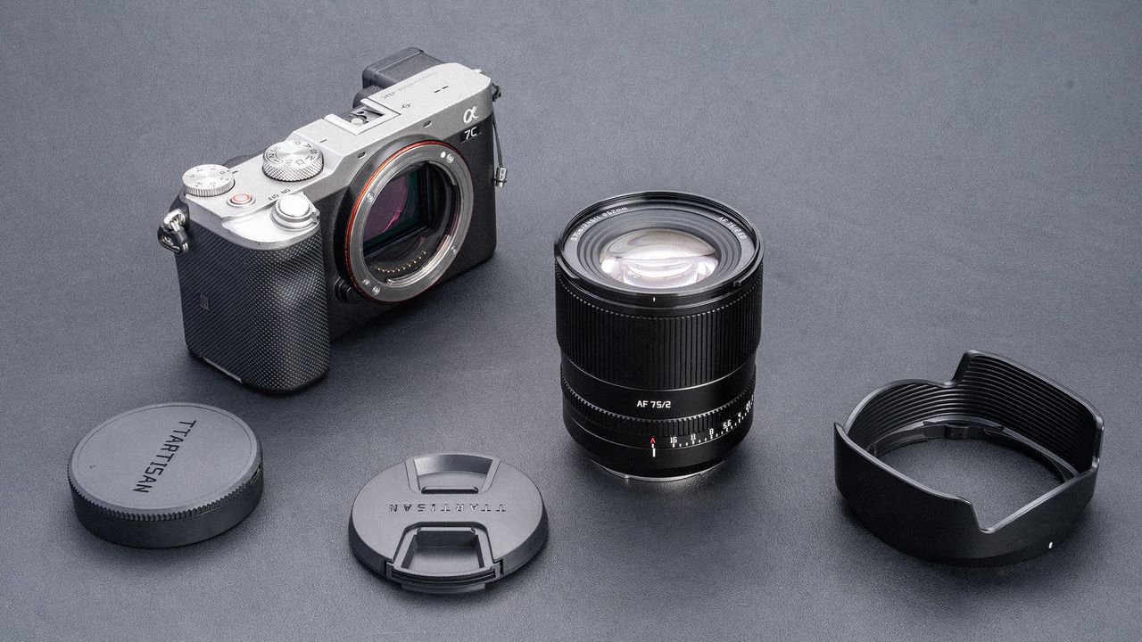 TTArtisan AF 75mm f/2 next to mirrorless camera, with lens hood, lens cap and rear lens cap on a grey surface