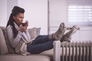 A woman sipping tea with her feet on an oil filled radiator