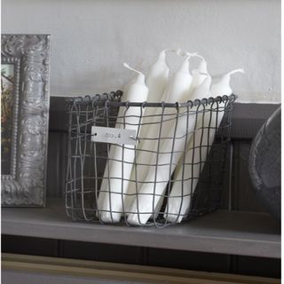 A wire storage basket full of fresh white candles and a shelf with a picture