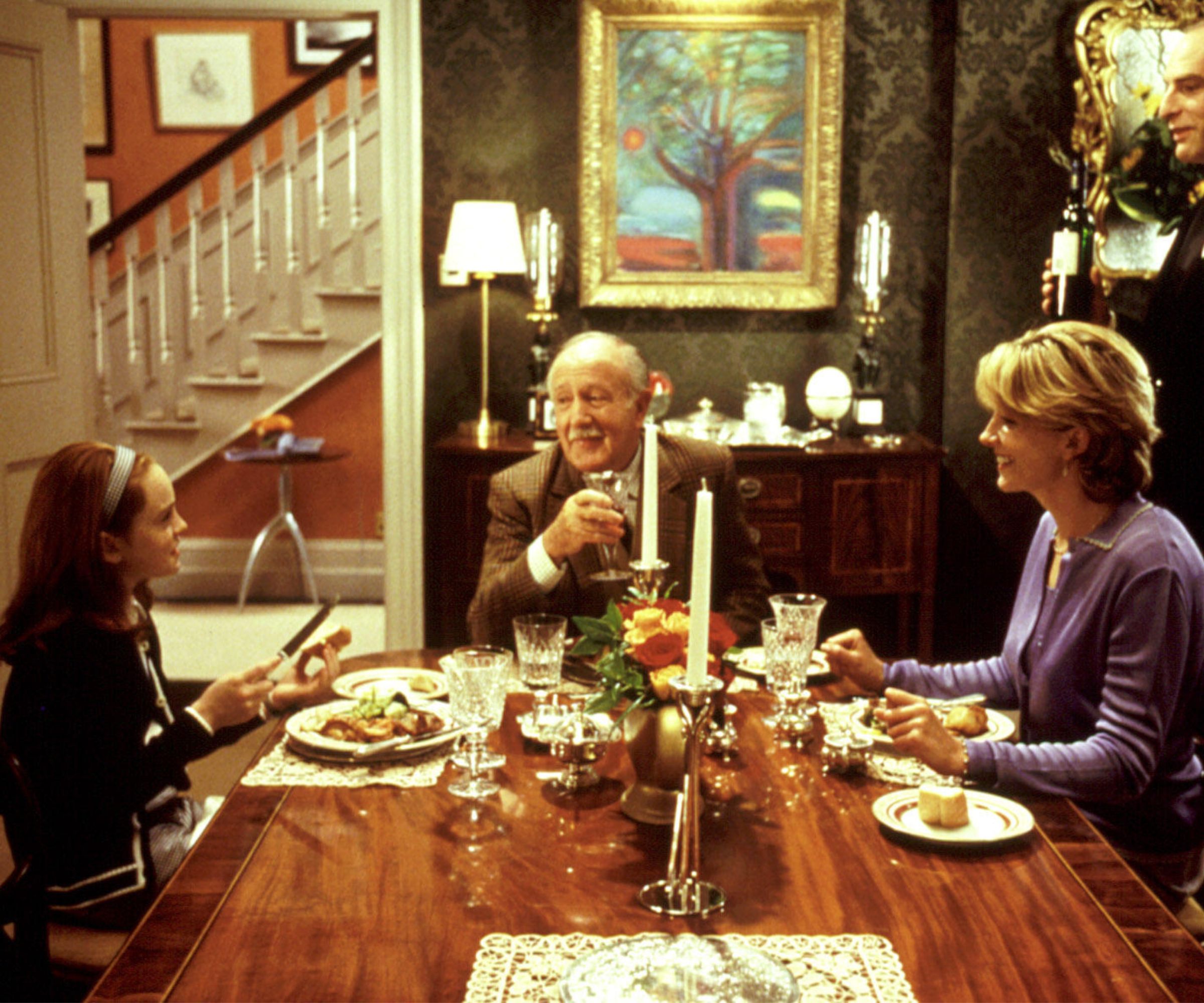 Lindsay Lohan and Natasha Richardson in a traditional dining room with painting, sconces, ornate mirror, and wood dining table with candles