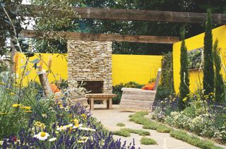 stone outdoor fireplace against yellow garden wall