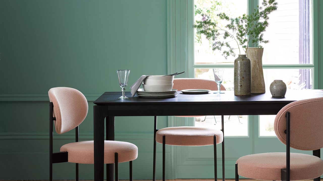 Green dining room with pink velvet chairs and black dining table