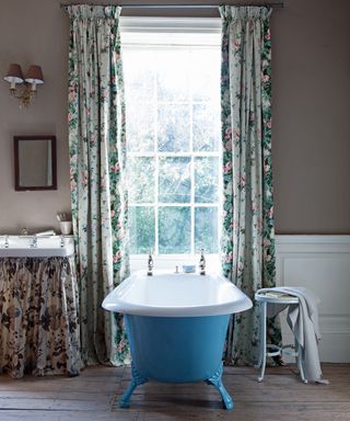 Bathroom with roll top bath with blue exterior, floral patterned curtains and floral curtain on vanity