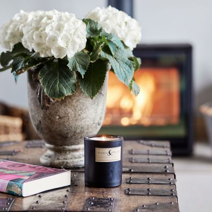 Lit candle and a vase of hydrangeas sitting on a coffee table in front of a log burner