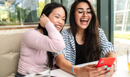 Portrait of happy lesbian couple in a restaurant having good time using cell phone. LGBTQ concept. Pride Month memes