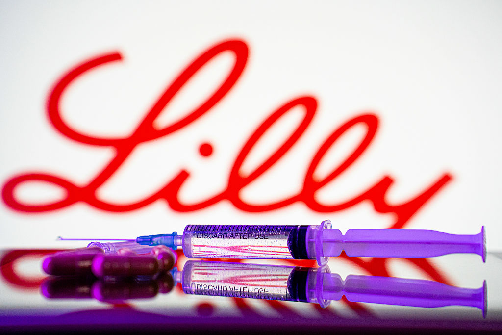 Healthcare stocks: A syringe and some pills are in front of the logo of Eli Lilly pharmaceutical company