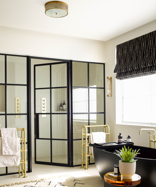 Black framed doors in a bathroom idea with brass towel rails, black and gold blind window treatment and black bath