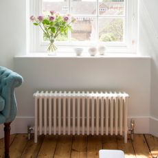 White radiator in a white living room, underneath a windowsill with a vase of flowers on it