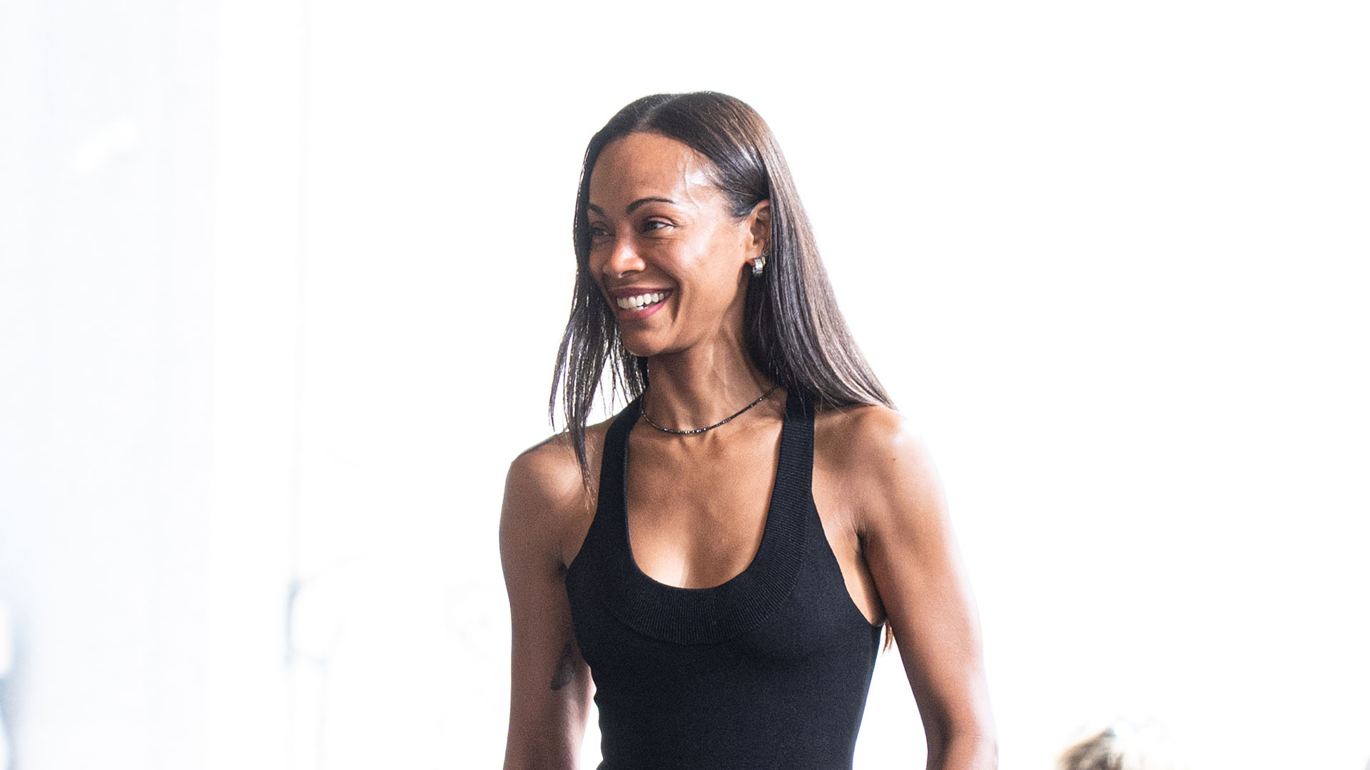 Zoe Saldana wearing a black tank top, bermuda shorts, and black flats