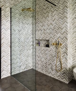 A walk in shower with zig zag marble tiling and an alcove used as a shelf