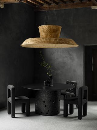 A large basket woven lampshade by Faina hanging over black round dining table and chairs