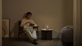 A man reads a book next to an illuminated Sony LSPX-S3 wireless speaker