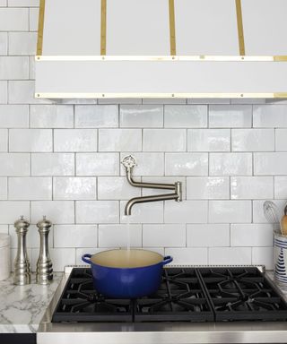 A kitchen with white tiled walls and a white hood with gold embellishments