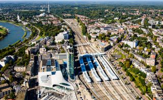 An aerial view of Arnhem Station with three train lines and a building next to them and a view of houses and trees around it.
