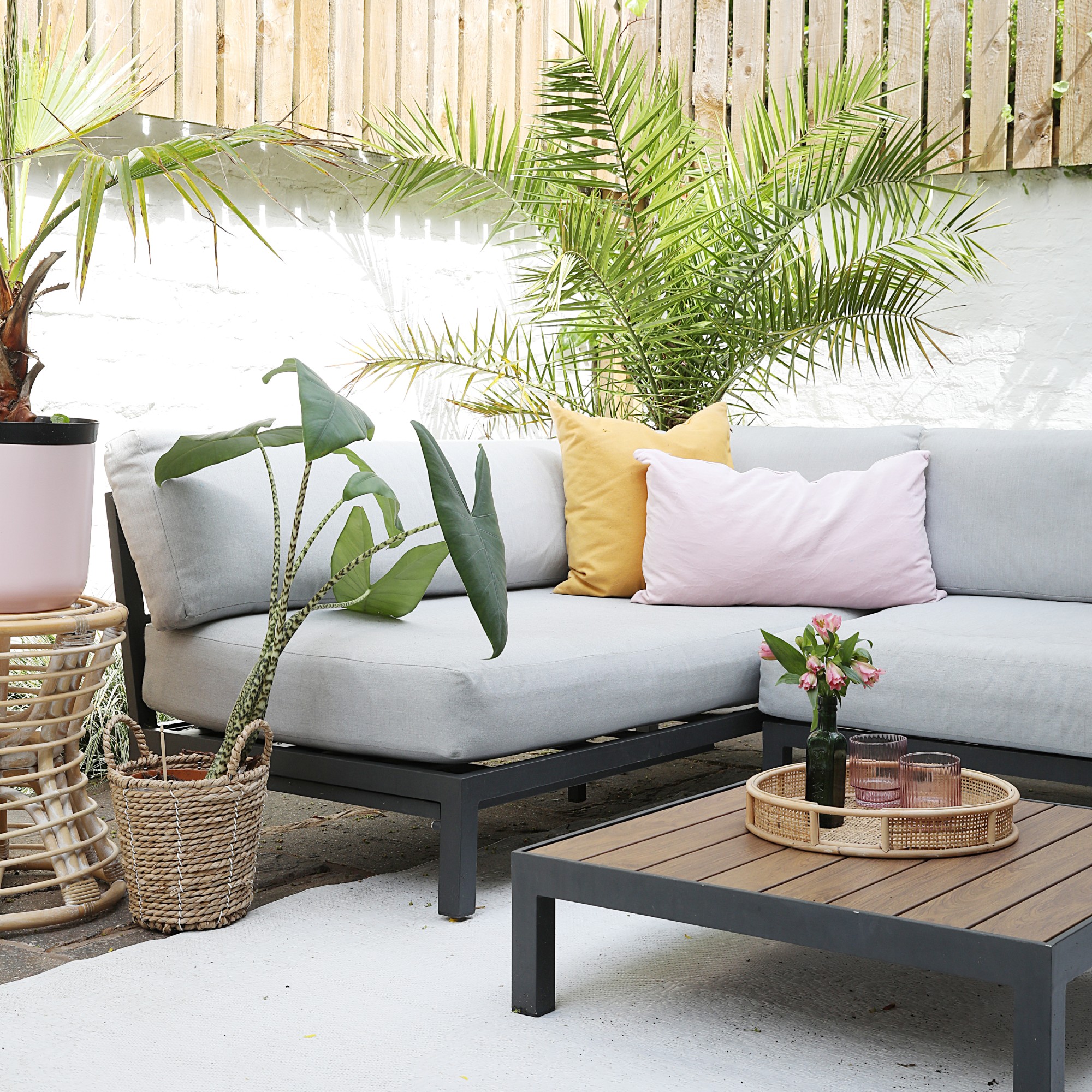 A garden with a corner outdoor sofa with grey cushions and a matching coffee table