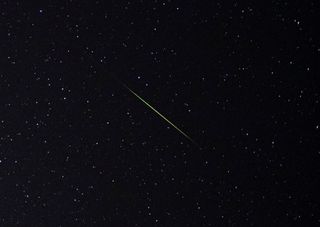 A close-up of a bright green and white perseid meteor streak through the star filled sky.