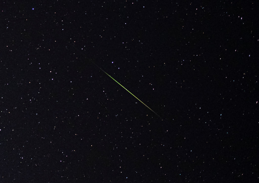 A close-up of the bright green and white Perseid meteor streaks through a star-filled sky.