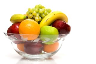 A fuit bowl filled with oranges, apples, grapes and bananas.