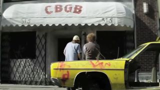 Alan Rickman and Donal Logue with their backs to the camera looking at CBGB awning in CBGB