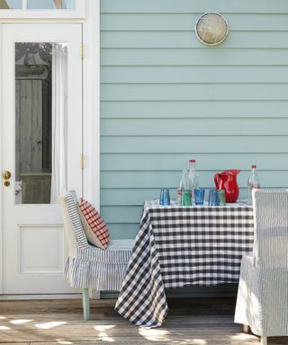 home exterior with light blue wood clad wall, outdoor dining table with gingham tablecloth and striped chairs