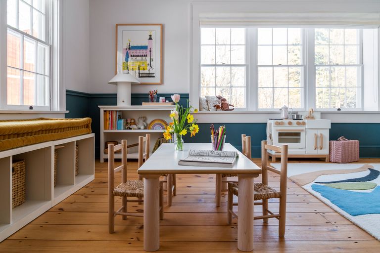 Playroom ideas featuring a small wooden table and chairs and play kitchen in a white room with dark blue skirting boards.