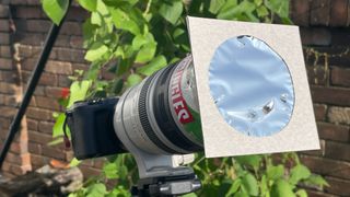 A camera points down through a pringles tube with a solar filter attached at the end.