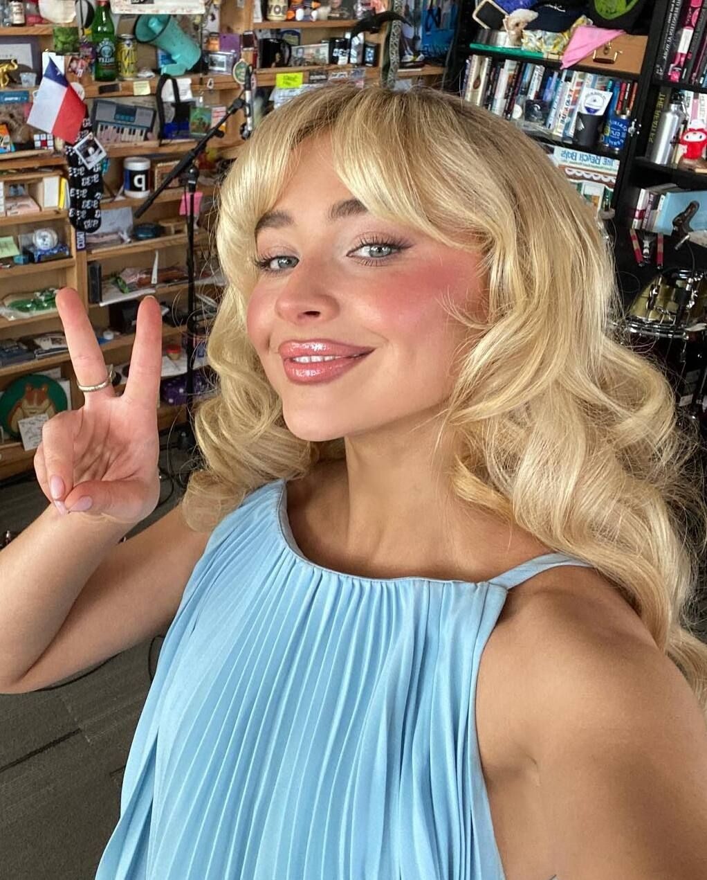 Sabrina Carpenter poses with blurred, pink cheeks in a blue pleated top