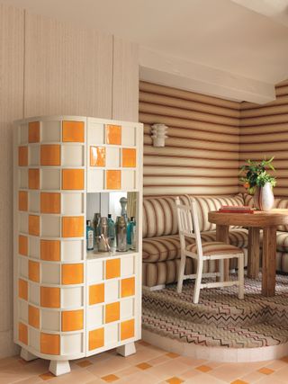 a small living room space with a tiled bar unit with orange and white checkerboard. striped banquette seating and walls are in the background